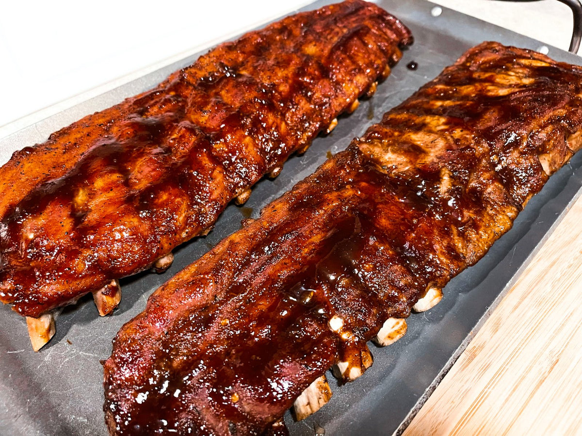 Two racks of smoked pork ribs glazed with Show-Me® Bar-B-Q Sauce on a sheet pan