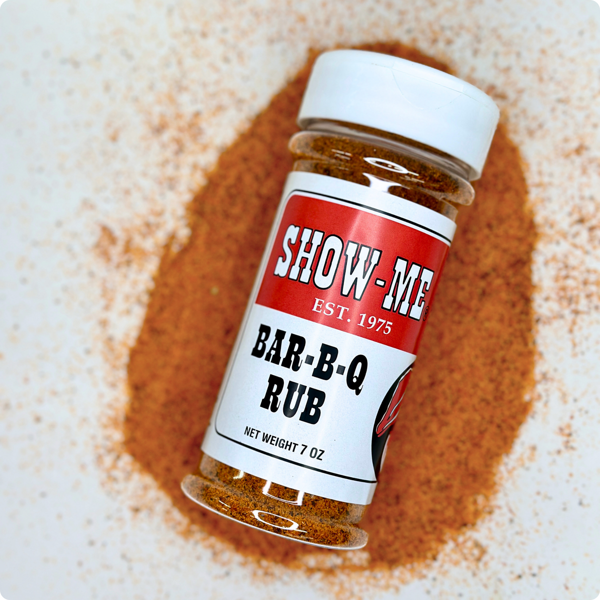 Show-Me® Bar-B-Q Rub 7 oz shaker lying on a pile of red-orange BBQ dry rub
