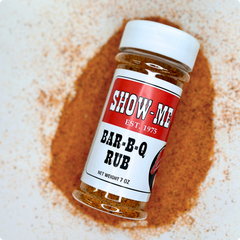 Show-Me® Bar-B-Q Rub 7 oz shaker lying on a pile of red-orange BBQ dry rub