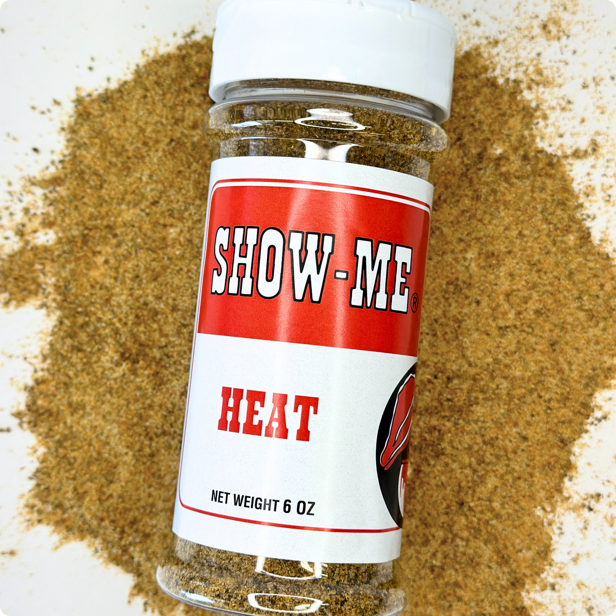 Show-Me® Heat Rub 6 oz shaker lying on a pile of the spicy seasoning blend