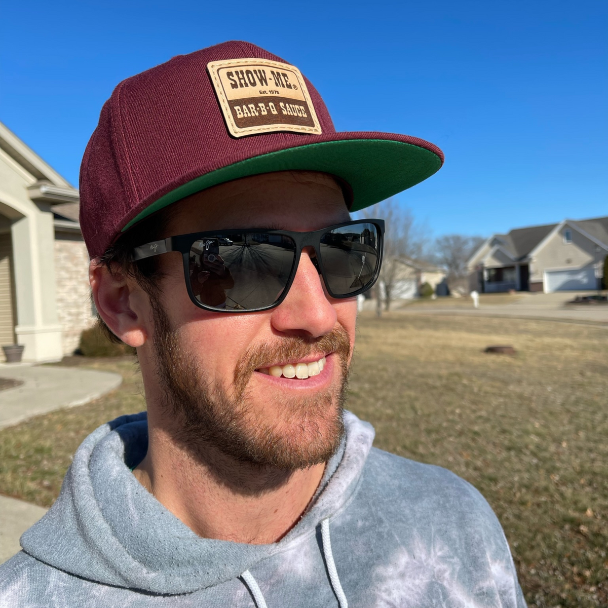 Man outdoors wearing the maroon Show-Me® Bar-B-Q Sauce hat with green under the visor